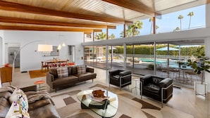 Un salon moderne avec une table basse en verre, des canapés en cuir et une vue sur une piscine et des palmiers.