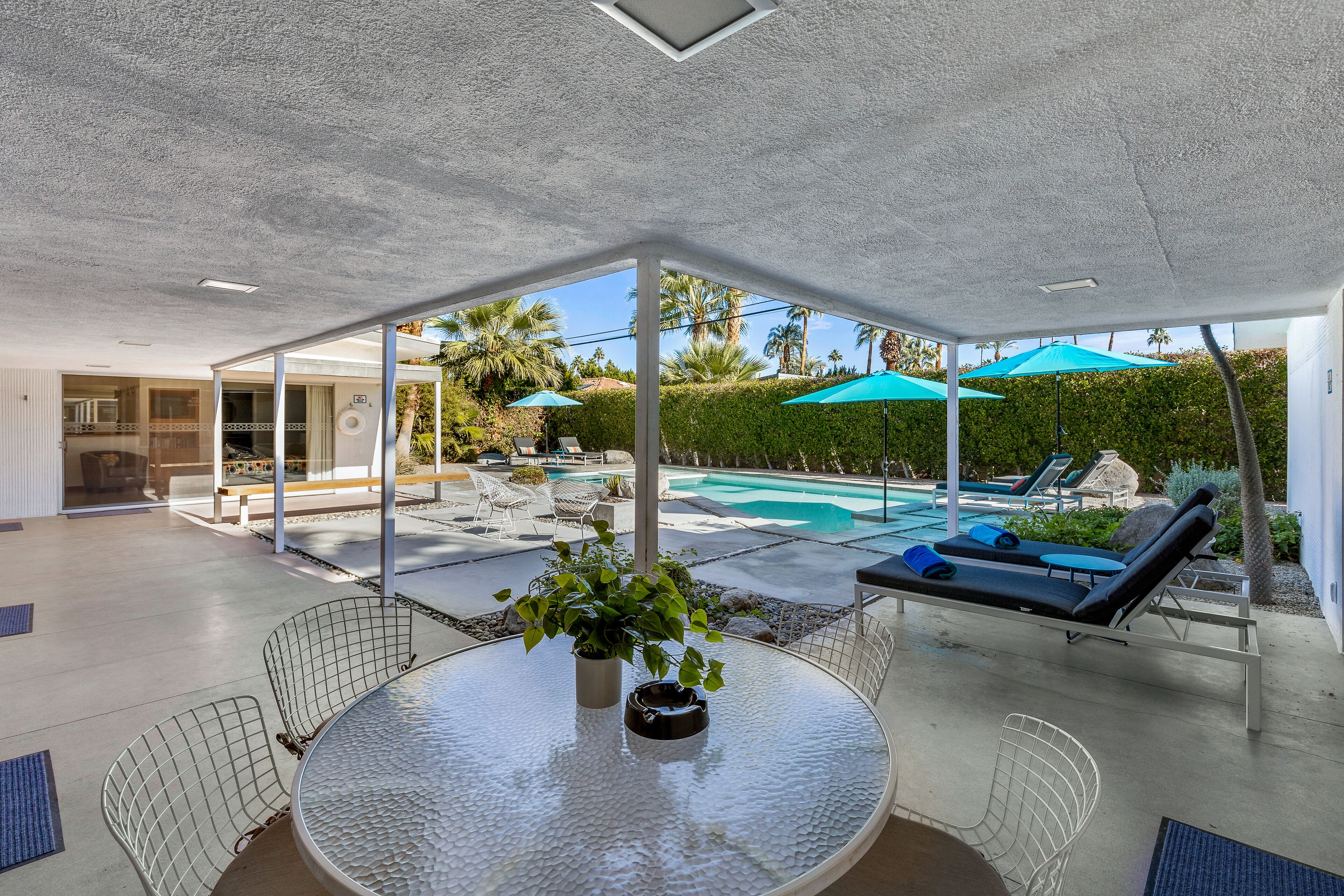 A modern outdoor patio with a glass enclosure, a pool, and lounge chairs.