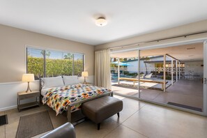 A bedroom with a bed, bedside tables, a bench, and a view of an outdoor patio with a pool and lounge chairs. - Deepwell Mid-Century Classic (Palm Springs)