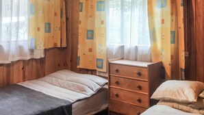 Een kleine, eenvoudige kamer met een eenpersoonsbed, een houten dressoir en gordijnen met een geometrisch patroon.