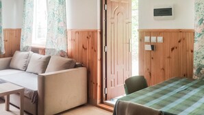 Een knus ingerichte kamer met een bank, een tafel en een stoel. Een houten deur en een raam met gordijnen.