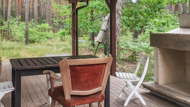 Een terras buiten met een houten tafel en stoelen, een pergola en een stenen open haard.
