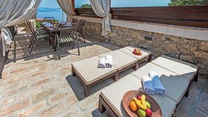 Un espacio al aire libre iluminado por el sol con dos sillones de descanso, una mesa con una bebida y un frutero.
