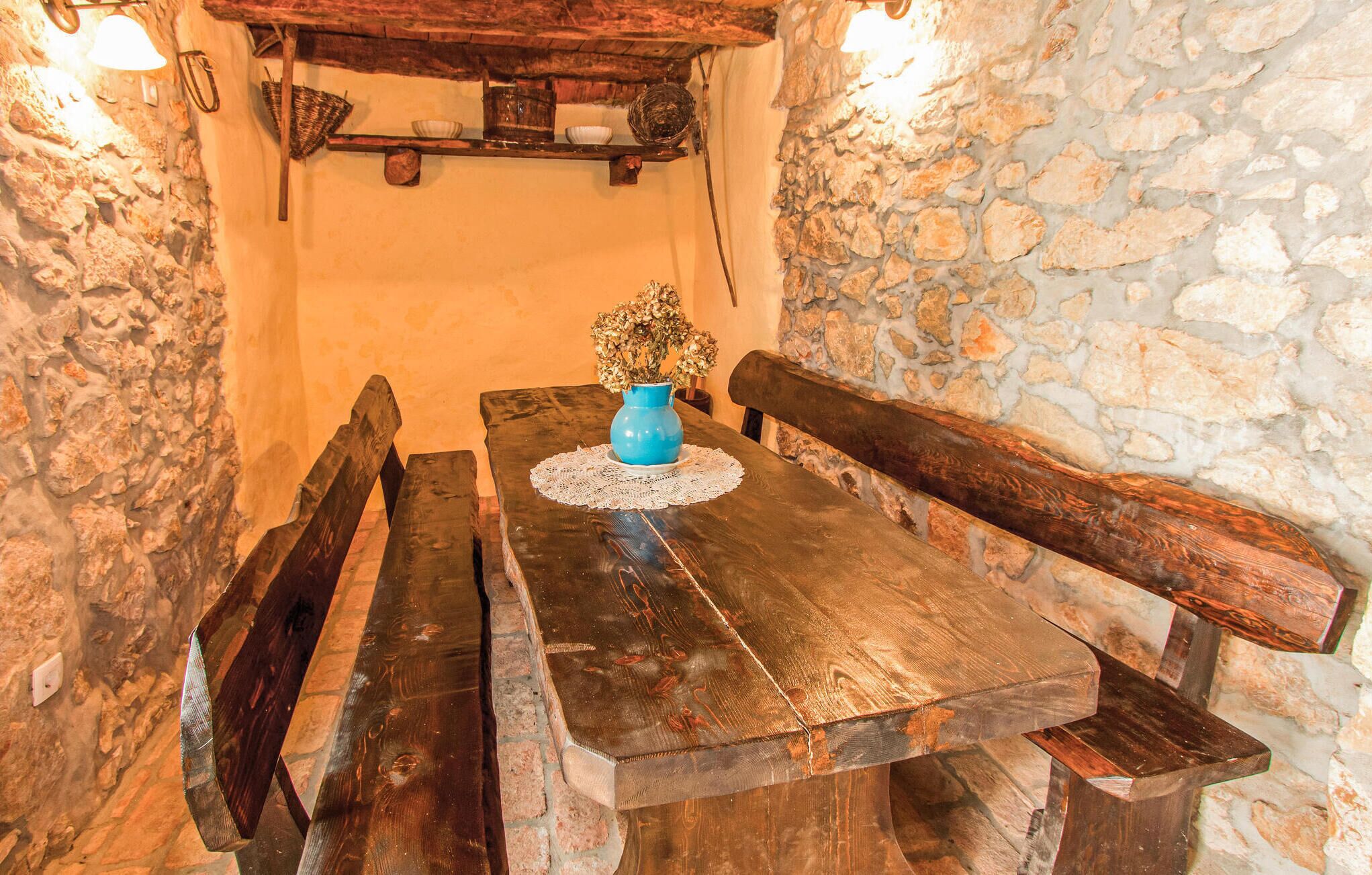 A rustic wooden table with benches, a blue vase with dried flowers, and a stone wall.