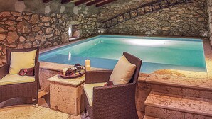 Un área interior con piscina de paredes de piedra, mobiliario de mimbre y una escalera de piedra.