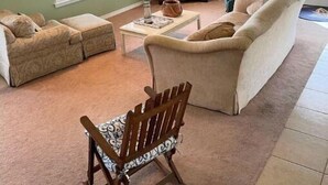 Un salon comprenant un canapé d’angle, un fauteuil à bascule en bois, une table basse et un ventilateur de plafond.