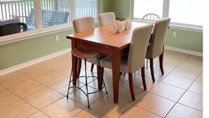 Un coin repas avec une table et des chaises en bois, de grandes fenêtres donnant sur une terrasse et des murs de couleur verte.