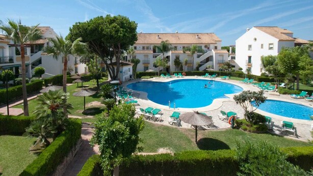 Resort com uma grande piscina cercada por palmeiras e espreguiçadeiras.