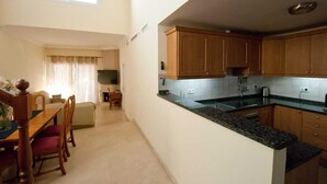 Uma cozinha compacta com armários de madeira, bancada de granito e uma área de refeições com mesa e cadeiras.