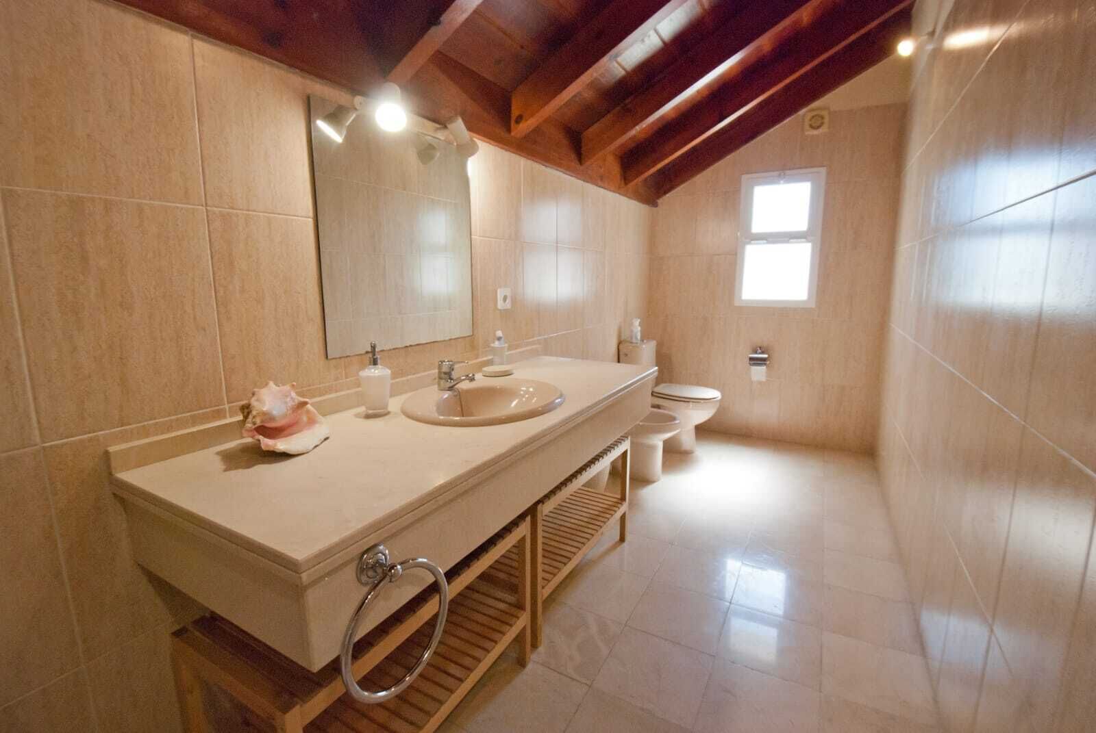 Et badeværelse med et stort spejl, to vaske, et toilet og et vindue.