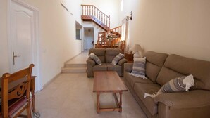 Uma sala de estar com sofá, uma mesa de madeira e escada para outro cômodo.
