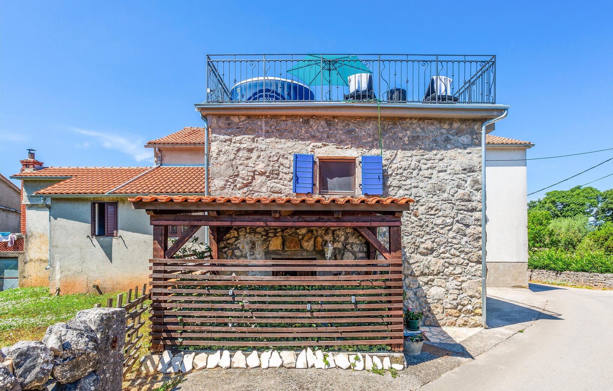 Un edificio in pietra con un balcone, una piccola finestra con persiane e una struttura in legno di fronte.