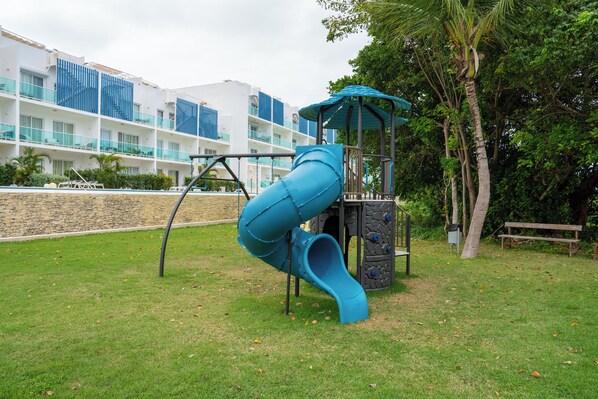 A playground with a blue slide, a climbing structure, and a bench.
