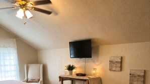 A bedroom with two beds, a ceiling fan, a television, a small table with a plant, and artwork on the wall. - Ouachita Spring Studio Stay- Sleeps 4 (Mena)