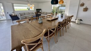 Un vaste espace dédié à la salle à manger, avec une grande table en bois, entourée de chaises en osier, et des luminaires suspendus au-dessus.