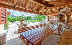 Une terrasse extérieure avec des bancs en bois, une cheminée en pierre et une vue sur un jardin et des montagnes.