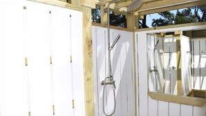 Une cabane en bois avec un espace douche comprenant un pommeau de douche et un miroir.