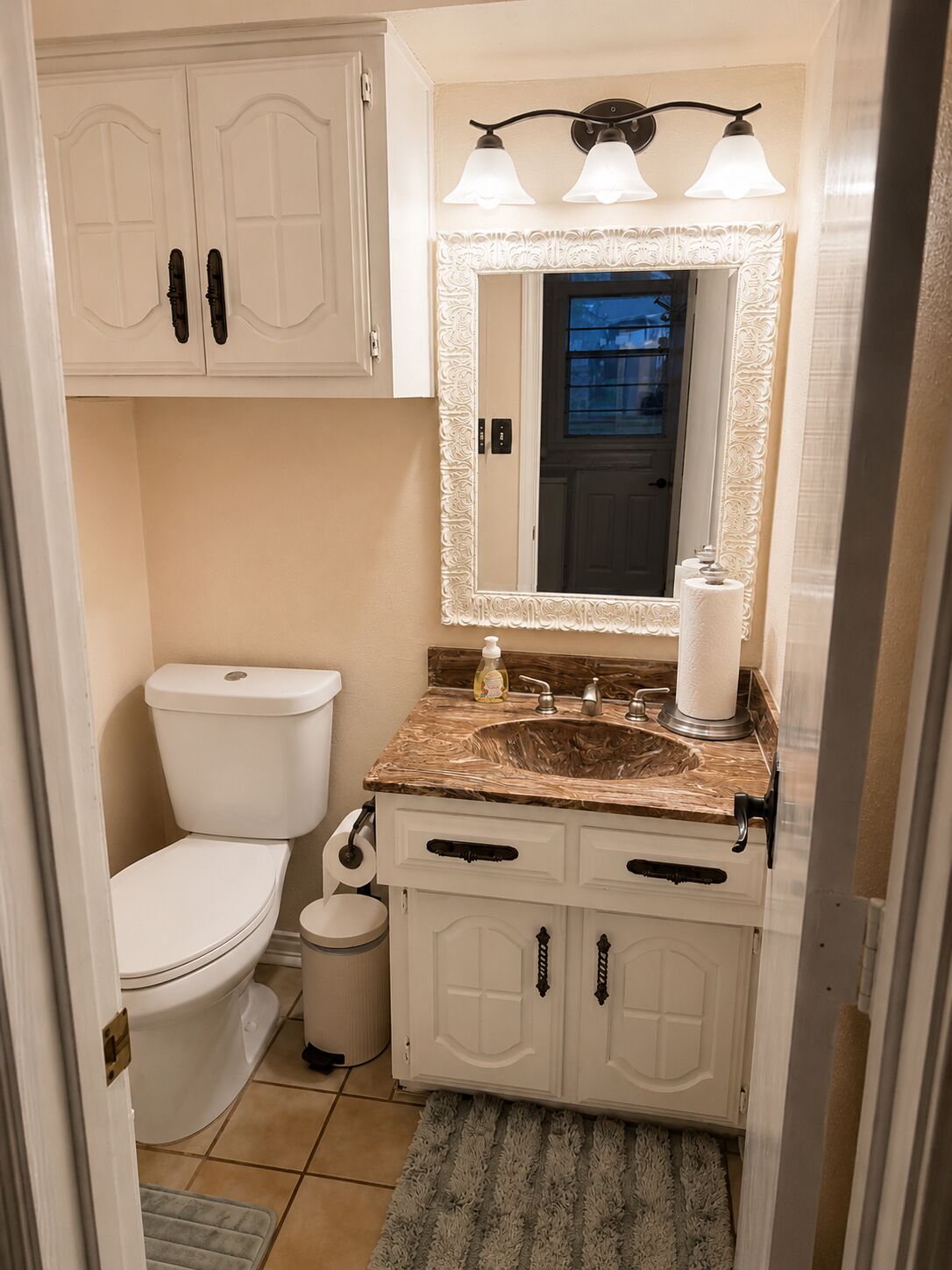 A bathroom with a toilet, sink, vanity, and a mirror with a decorative frame.