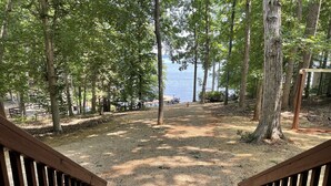 A wooden deck leading to a gravel area with trees and a view of a body of water.