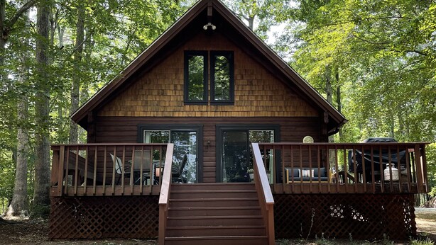 A wooden cabin with a deck and stairs leading to a large window.