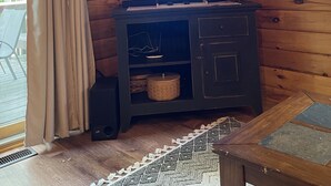 A wooden cabin interior with a television mounted on the wall, a dark wooden cabinet below, and a window with curtains.