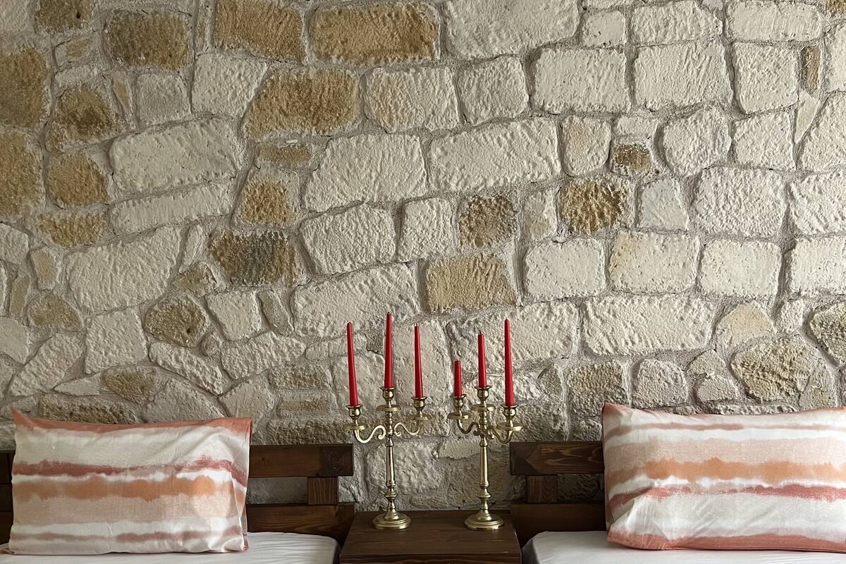 A room with two beds, a stone wall, and a candelabra with candles.