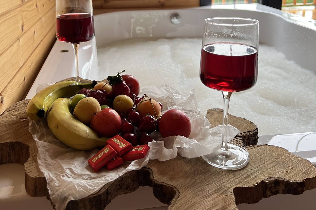 A wooden interior with a hot tub, fruit, and two glasses of red wine on a wooden table.