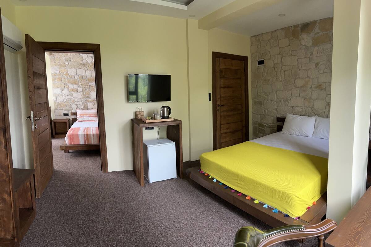 A bedroom with a bed, a television, a small refrigerator, and a stone wall.