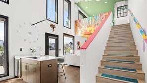 Una cocina moderna con una isla central, una escalera con barandillas coloridas y un mural vibrante en la pared.