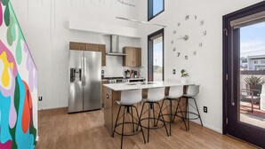 Una cocina moderna con refrigerador de acero inoxidable, armarios de madera y una isla blanca con taburetes de bar.