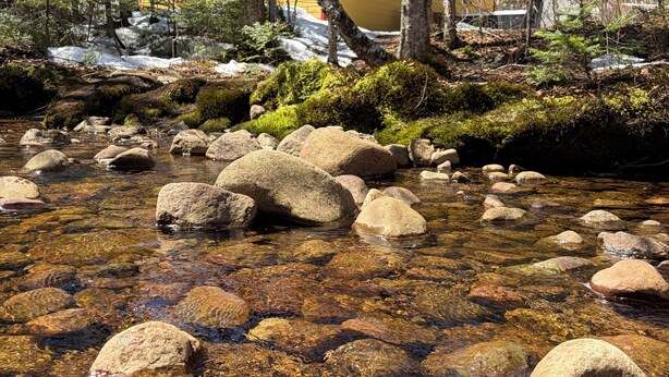 A clear stream with rocks, surrounded by trees and a yellow building with a red roof. - 5 minutes from the Bras du Nord Valley / Chalet with riverfront spa (Saint-Raymond)