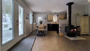 A cozy living room with a fireplace, a dining area with wicker chairs, and a kitchen with wooden cabinets. - 5 minutes from the Bras du Nord Valley / Chalet with riverfront spa (Saint-Raymond)