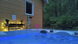 A hot tub with blue lighting, a pink glass, and a wooden deck with lights. - 5 minutes from the Bras du Nord Valley / Chalet with riverfront spa (Saint-Raymond)