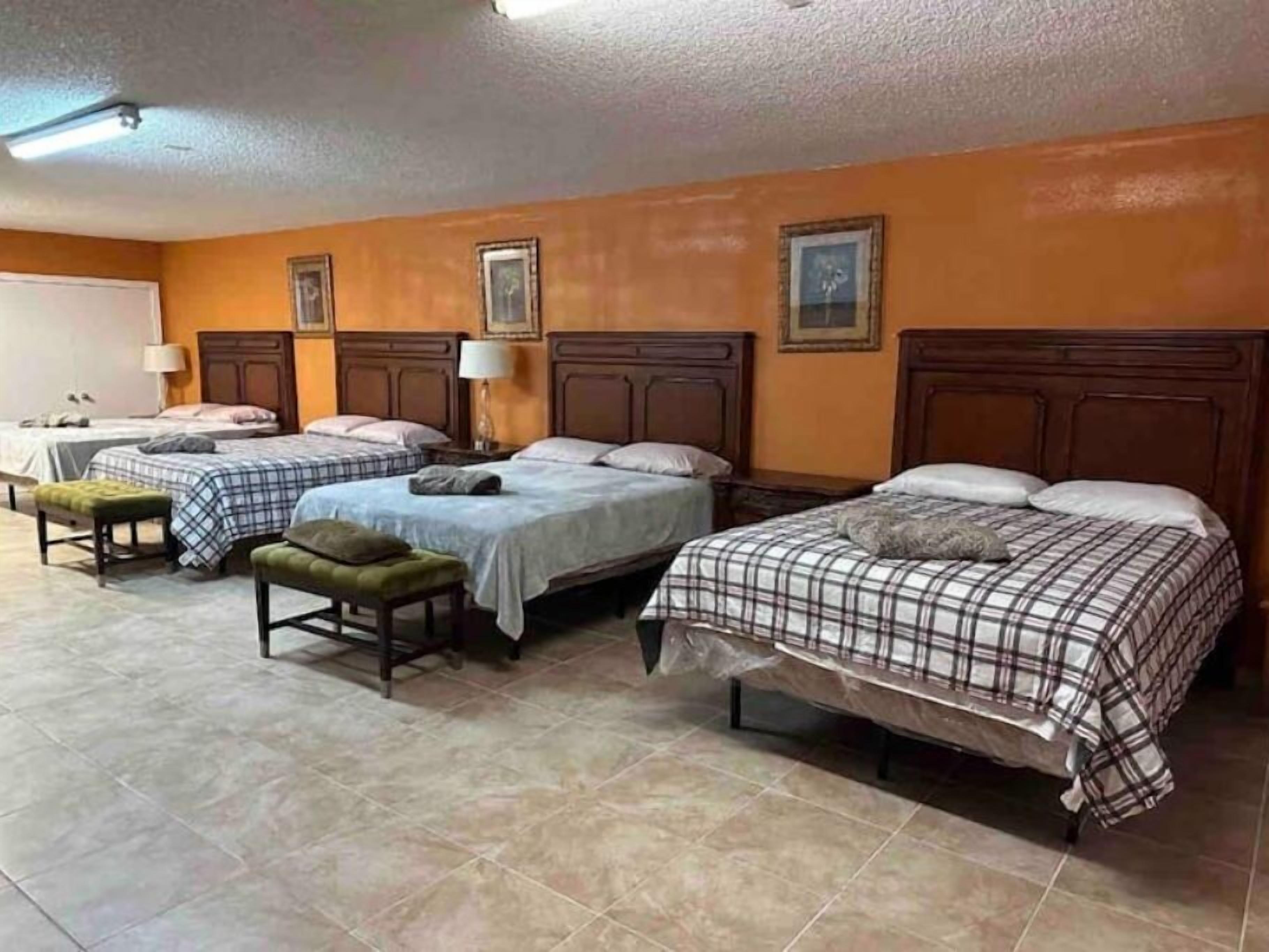Une chambre d’hôtel avec trois lits, chacun doté d’une tête de lit en bois et d’une couverture à carreaux. La chambre comprend également un banc et une petite table.