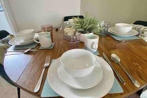 Enjoy meals with family and friends at this dining table for four, complete with fine china and a potted plant.
