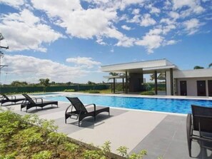 Ein moderner Poolbereich mit Liegestühlen, einer überdachten Lounge und blauem Himmel.