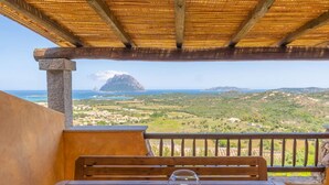 Ein Holztisch mit einem Glaslaternenhalter und einer Tischmatte, mit Blick auf eine Küstenlandschaft mit Berg und Gebäuden.