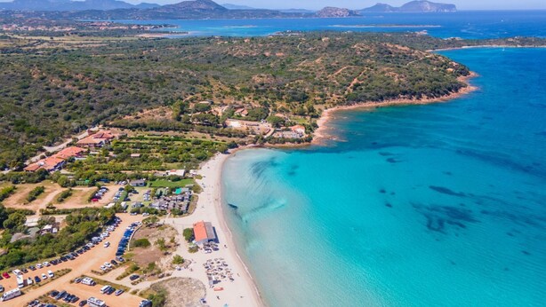 Vue aérienne d’une zone côtière avec une plage, des parkings et des bâtiments.