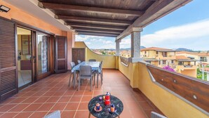 Un balcon doté d’un plafond en bois, une table avec des chaises et une vue sur des bâtiments situés au loin.