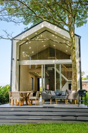 Une maison moderne dotée d’une façade en verre, d’un espace extérieur aménagé et d’un escalier menant à un niveau supérieur.