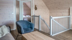 Une pièce avec un plafond en bois, une chaise bleue, une table en bois et un lit recouvert d’une couvre-lit blanche à motifs.