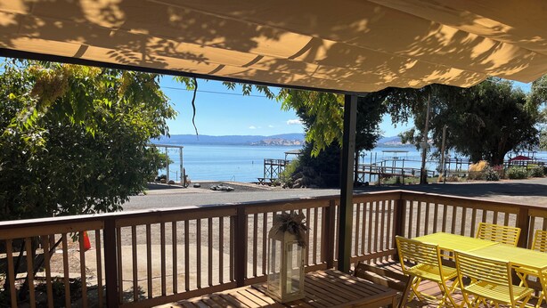 A wooden deck with yellow chairs and tables, overlooking a body of water and distant mountains. - ALL INCLUSIVE AMENITIES:Kayak,SUP,Pedal Boat,PingPong,Pickleball,Movie Nt &MORE! (Nice)