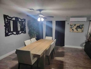 A dining area with a wooden table, white chairs, a ceiling fan, and a world map on the wall.