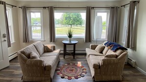 Ein Wohnzimmer mit zwei Sofas, einem kleinen Tisch mit einer Pflanze und Blick auf eine grüne Landschaft durch große Fenster.