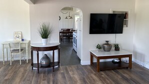 Ein modernes Wohnzimmer mit an der Wand montiertem Fernseher, ein Essbereich mit Tisch und Stühlen sowie ein Flur zum Küchenbereich.