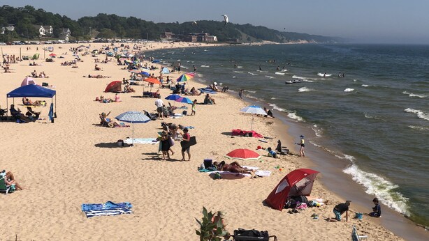 Ein belebter Strand mit Sonnenschirmen, Badegästen und freiem Blick auf das Meer.