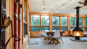 A cozy cabin interior with a dining area, a fireplace, and large windows offering a view of the forest.