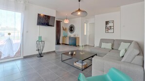 A modern living room with a grey sofa, a glass coffee table, and a TV mounted on the wall.