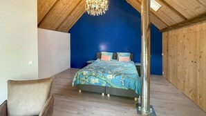 Ein Schlafzimmer mit schrägverdeckter Decke, einem Bett mit floralem Bettzeug, einer Chandelieber und Holzwänden.