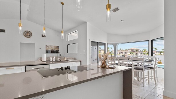 Una cocina moderna con una isla grande, iluminaci ón colgante y vistas a una piscina y zona de estar exterior.